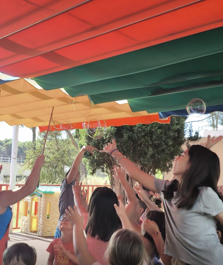 Espectáculo de pompas de jabón gigantes frente a un libro de "La Pequeña Oruga Glotona" y juguetes de exterior.