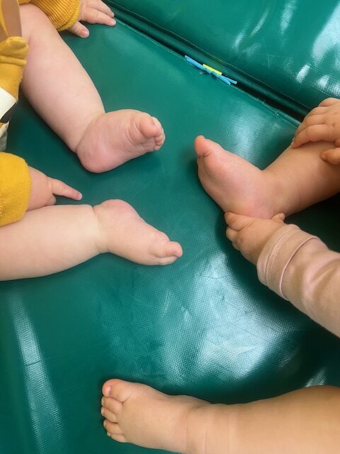 Primeros planos de los pies de varios bebés de 0 a 1 año compartiendo un espacio de juego y masajes sobre colchonetas en la Escuela Infantil La Casita.