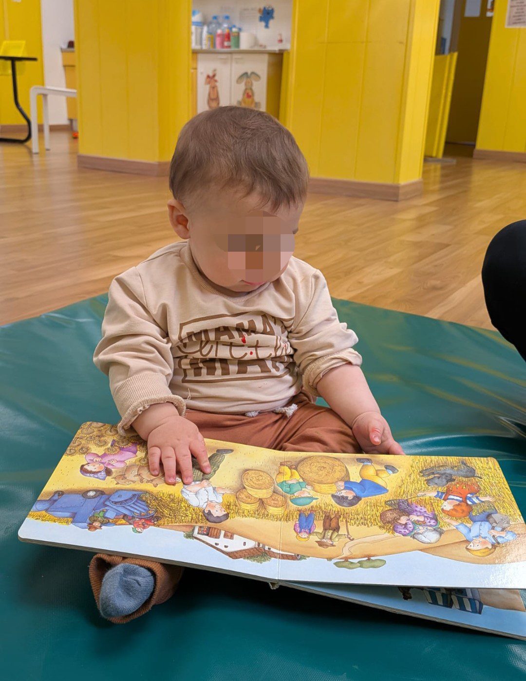 Bebé sentado sobre colchonetas en un aula amplia y segura de la Escuela Infantil La Casita de Torrejón explorando un cuento ilustrado.