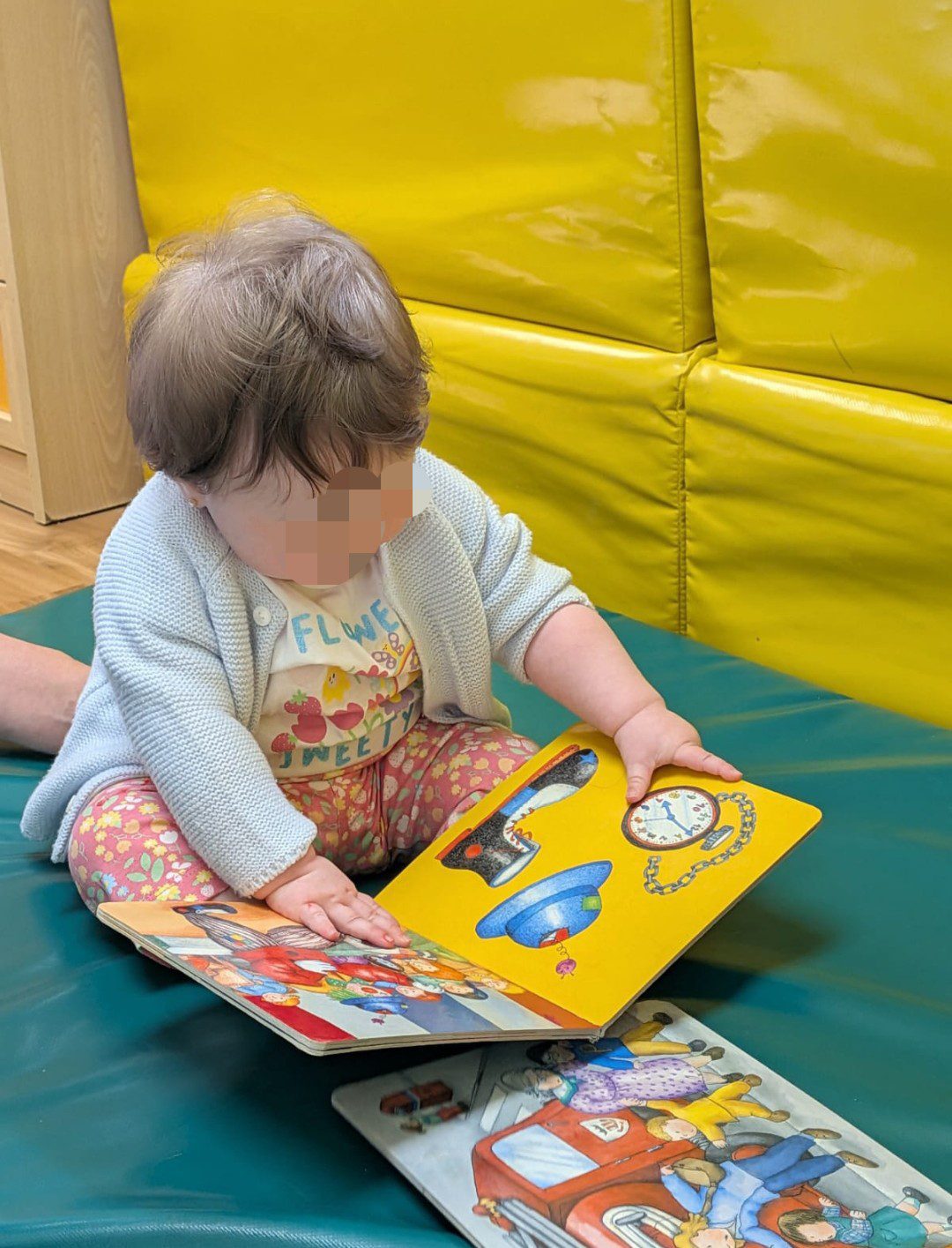 Bebé sentado cómodamente explorando un libro de ilustraciones coloridas en el aula de la escuela infantil La Casita.