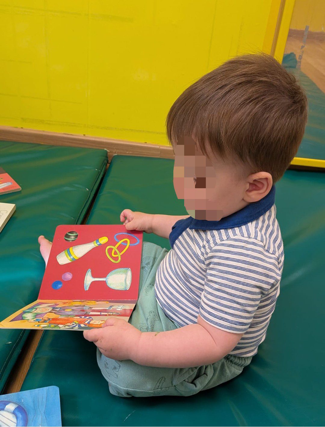 Bebé sentado en el rincón de lectura explorando de forma autónoma un libro de imágenes.