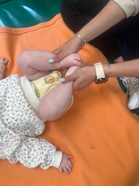 Primer plano de técnica de masaje abdominal y de piernas para aliviar cólicos en bebés, realizada por una profesional de la Escuela Infantil La Casita.