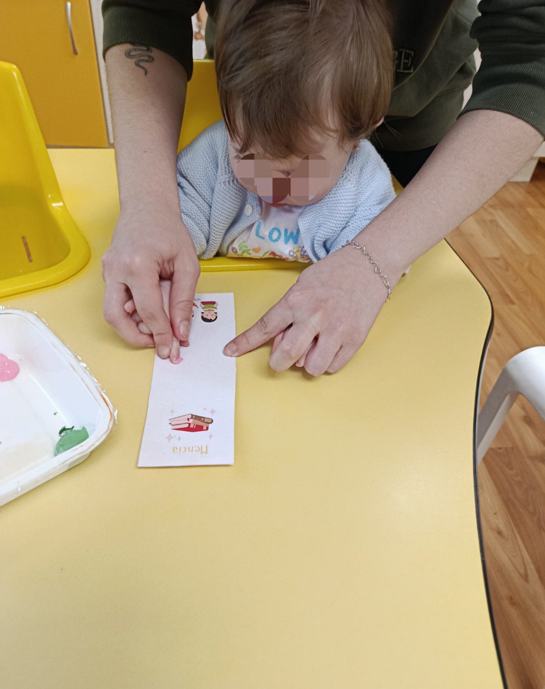 Educadora guiando la mano de un bebé para estampar pintura en un taller de manualidades.