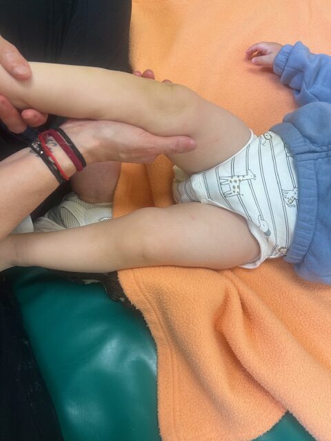 Primer plano de una educadora infantil realizando un masaje relajante en la pierna de un bebé durante un taller de estimulación en la Escuela Infantil La Casita.