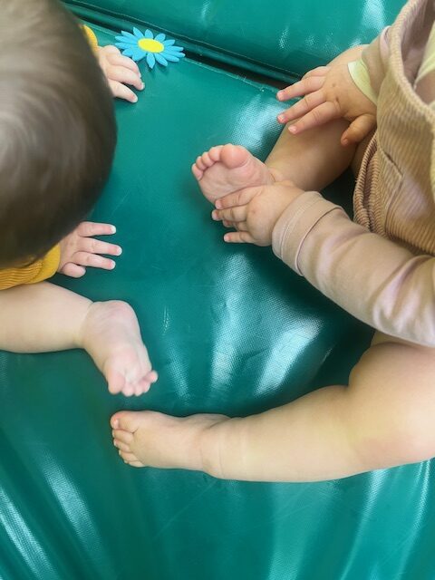 Varios bebés de 0 a 1 año interactuando y jugando sobre colchonetas verdes durante una sesión grupal en la Escuela Infantil La Casita.