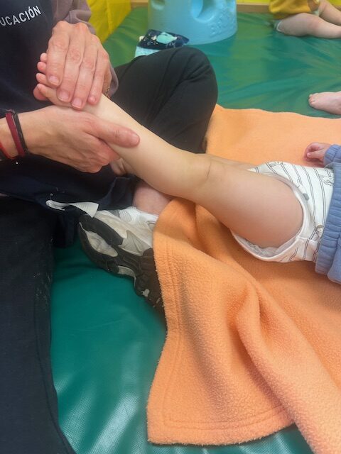 Una educadora infantil realiza un masaje suave en el pie y la pierna de un bebé de 0 a 1 año sobre una colchoneta en la Escuela Infantil La Casita.